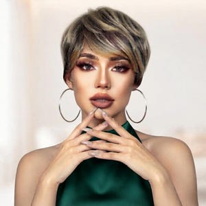 Pode incluir: Uma peruca curta de corte pixie em camadas com uma mistura de tons loiro acinzentado e castanho escuro. O cabelo é estilizado com franja lateral e volume no topo. Grandes argolas douradas finas e um top verde escuro sem mangas.