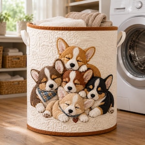 May include: A cylindrical laundry hamper made of cream-colored quilted fabric with a brown trim and two side handles. The front features a detailed applique of five sleeping Corgi puppies in various shades of brown, black, and white.