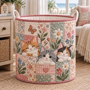 May include: A cylindrical fabric storage basket featuring a quilted patchwork design with floral patterns and three embroidered kittens. The kittens are depicted in orange tabby, gray tabby, and calico colors, surrounded by flowers and a butterfly.
