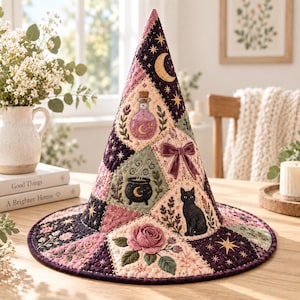May include: A conical hat featuring a quilted patchwork design in shades of purple, pink, and cream. The fabric displays embroidered motifs including a black cat, a potion bottle, a cauldron, a rose, stars, moons, and a velvet bow accent.