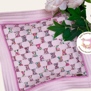 Könnte beinhalten: Ein rosa Kissen mit einem gewebten Blumenmuster und einem rosa Rand. Das Kissen ist von einer rosa Blume und grünen Blättern umgeben. Das Bild enthält auch ein kreisförmiges Logo mit dem Text "PDF Sewing Pattern Sallieann Harrison - Quilter".