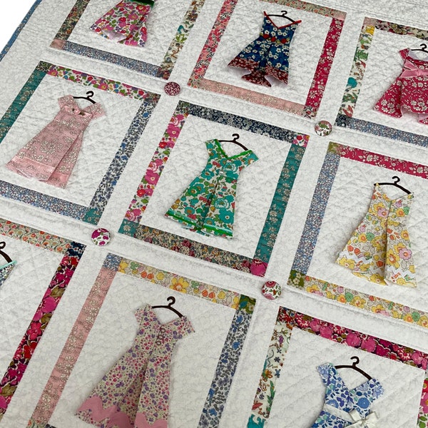 Puede incluir: Un edredón hecho a mano con vestidos de tela aplicados en varios estampados florales. Los vestidos están dispuestos en un patrón de cuadrícula, cada uno enmarcado por un borde de tela contrastante. El edredón es blanco con un patrón de diamantes acolchados y pequeños botones cubiertos de tela.