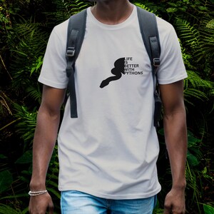 Peut inclure: Un t-shirt blanc à manches courtes avec une silhouette noire de serpent et le texte "LIFE IS BETTER WITH PYTHONS" imprimé sur la poitrine. Le t-shirt est porté avec un sac à dos gris foncé à bretelles noires et un jean bleu clair.