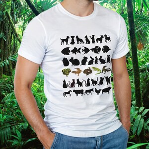 Peut inclure: Un t-shirt blanc à manches courtes avec une impression graphique de diverses silhouettes d'animaux et d'illustrations colorées disposées en rangées, incluant des chiens, poissons, petits mammifères, reptiles, chats, cheval, vache, âne, poule et cochon.