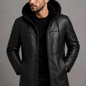 May include: A black leather jacket featuring a hood lined with black fur, a full-length front zipper, long sleeves, and two side pockets. The jacket has a smooth finish and horizontal seam detailing across the chest and torso area.