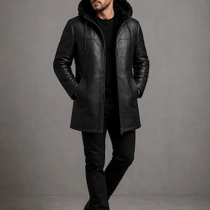 May include: A black leather hooded coat featuring a smooth exterior finish, a front zipper closure, and a plush dark interior lining. The coat includes long sleeves, two side pockets, and a drawstring hood, worn over a black shirt and black trousers.
