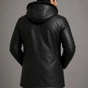 May include: A black leather jacket featuring a hood lined with black faux fur. The jacket has a smooth finish with visible horizontal and vertical seam detailing across the back, long sleeves, and a straight hemline that reaches the upper thighs.