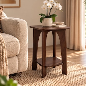 Pode incluir: Uma mesa lateral de madeira castanho-escura com um tampo quadrado e uma prateleira inferior. A mesa apresenta quatro pernas com recortes em arco que ligam o tampo à base, proporcionando uma estrutura estável para exibir objetos.