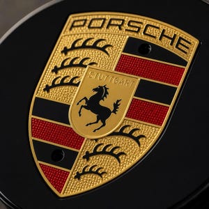 May include: A Porsche emblem featuring a shield design with a gold, black, and red color scheme. The crest displays the word PORSCHE at the top, the word STUTTGART in the center, and a black horse silhouette on a gold background.