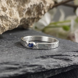 May include: A silver ring with a hammered texture and a small blue gemstone set in the centre.
