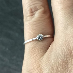 Può includere: Un semplice anello d'argento con una piccola pietra preziosa trasparente.
