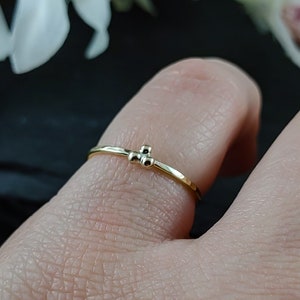 May include: A delicate gold ring with three small beads clustered together. The ring is worn on a person's finger.