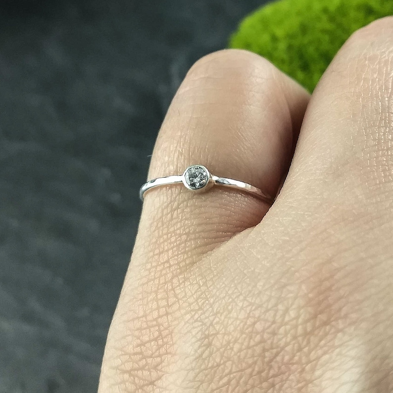 May include: A simple silver ring with a small, clear gemstone set in the centre. The ring band is hammered for a textured look.