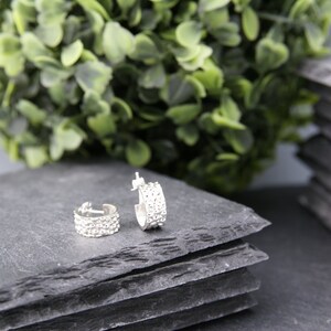 May include: Two silver hoop earrings with a row of small, clear rhinestones on each hoop. The earrings are on a gray slate surface.