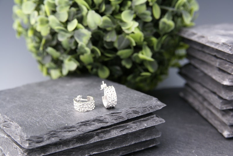 May include: Two silver hoop earrings with a row of small, clear rhinestones on each hoop. The earrings are on a gray slate surface.