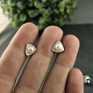 May include: A pair of silver triangle stud earrings with a white pearl in the center of each triangle.