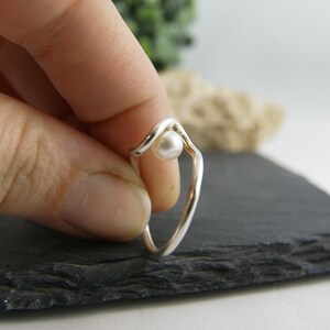 May include: A silver ring with a white pearl set in a wave-like design.