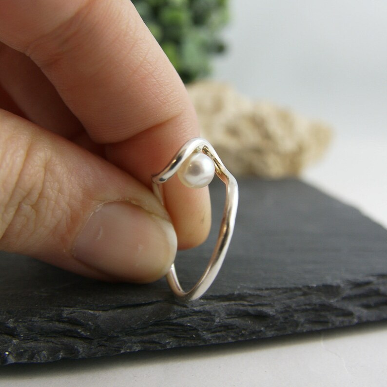 May include: A silver ring with a white pearl set in a wave-like design.