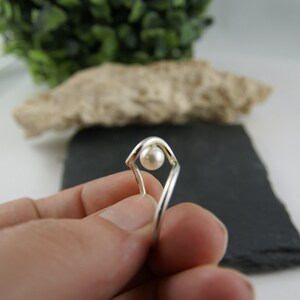 May include: A silver ring with a single white pearl set in a geometric design.