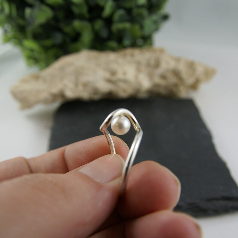 May include: A silver ring with a single white pearl set in a geometric design.