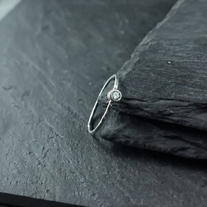 May include: A simple silver band ring with a single, small, clear gemstone.