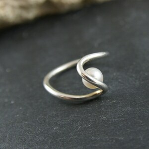 May include: A silver ring with a single white pearl set in the center. The ring is made of two bands that are intertwined.