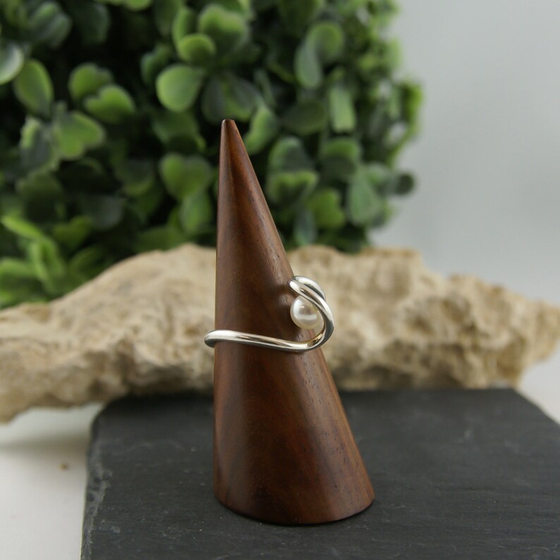May include: A silver ring with a single white pearl set in a curved band.