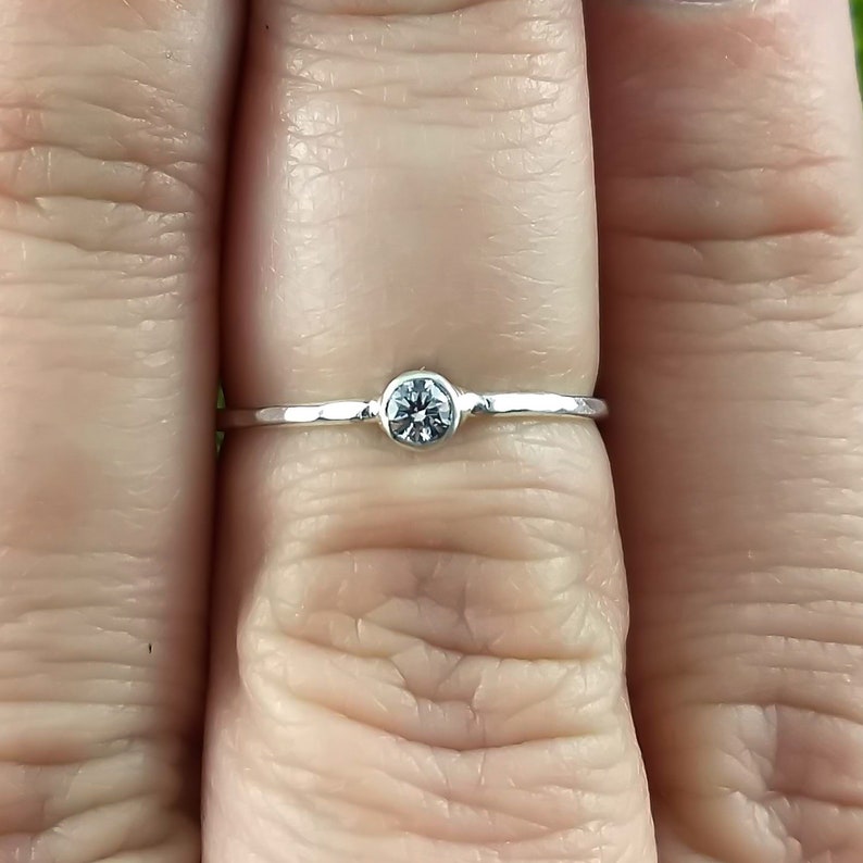 May include: A simple silver band ring with a small, clear gemstone in the centre.