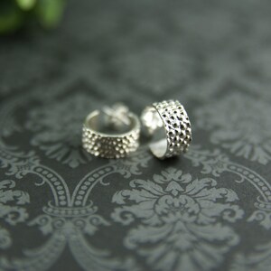 May include: Two silver ear cuffs with a textured, hammered finish. The cuffs are open and have a rounded shape.