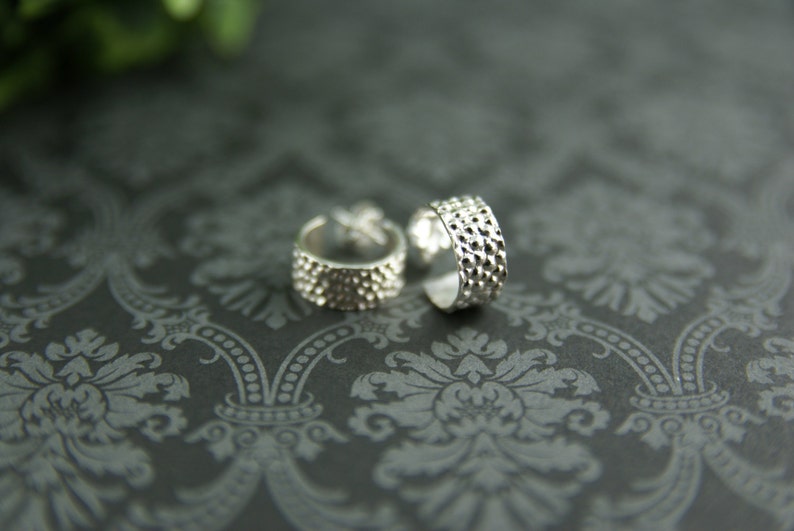 May include: Two silver ear cuffs with a textured, hammered finish. The cuffs are open and have a rounded shape.
