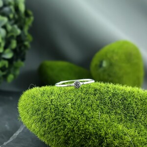 May include: A simple silver band ring with a single, small, round, dark grey gemstone.