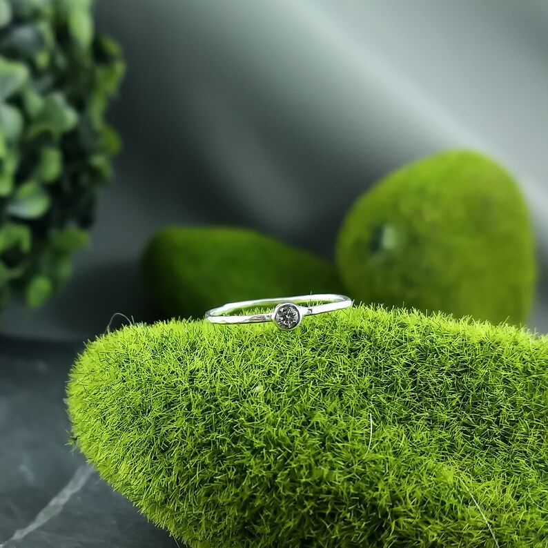 May include: A simple silver band ring with a single, small, round, dark grey gemstone.