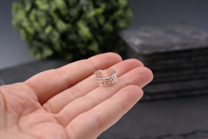 May include: A silver ear cuff with a textured, bumpy surface. The cuff is open and ready to be worn.