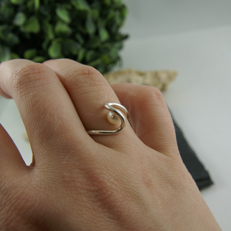 May include: A silver ring with a single pearl set in the center. The ring is designed in a wave shape.