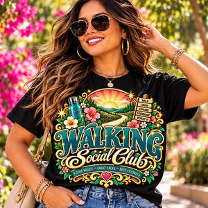 May include: A black t-shirt featuring a colorful graphic with the text Walking Social Club, Good Walks, Great Talks, Best Friends, and a signpost reading Walk, Laugh, Explore, Friendship, Repeat, surrounded by flowers and a water bottle.