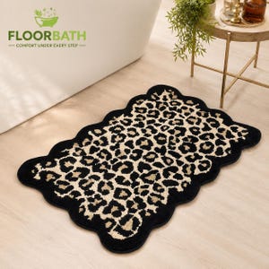 May include: A rectangular bath mat with a scalloped edge featuring a black and beige leopard print pattern. The mat displays the text FLOORBATH COMFORT UNDER EVERY STEP in the upper left corner, accompanied by a green bathtub icon.