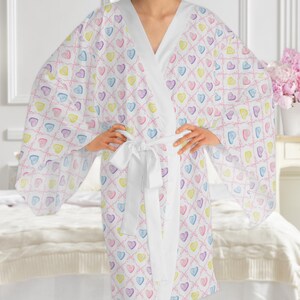 May include: White robe with a colorful heart pattern. The robe has long sleeves and a tie belt.