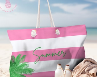 May include: A pink and white striped tote bag with the word "Summer" in green script. The bag features a palm tree graphic and white rope handles. Two small white bottles and a beige towel are on the sand.