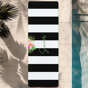 May include: A black and white striped beach towel with a floral design and the word "Summer" in green script. The towel is rectangular and appears to be made of a soft material, perfect for lounging by the pool or at the beach.