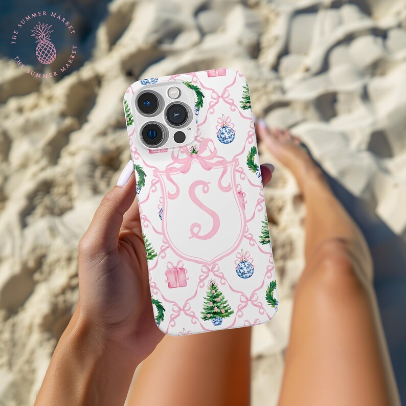 May include: White phone case with a pink Christmas-themed pattern. The design includes pink bows, Christmas trees, ornaments, and gift boxes. A pink letter "S" is centered on the case. The Summer Market logo is in the upper left corner.