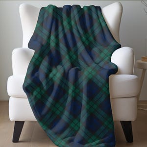 May include: A blue and green tartan blanket draped over a white armchair. The blanket displays a traditional plaid design with intersecting lines of dark blue, green, and black. The soft blanket adds comfort and style to any living space.