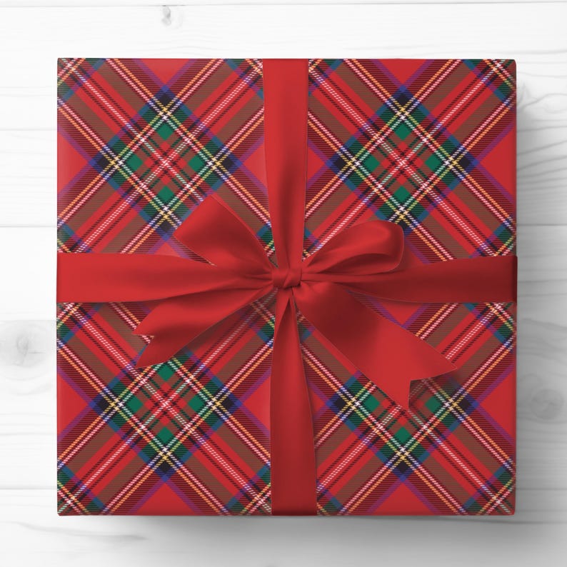 May include: A wrapped gift with red plaid wrapping paper and a red satin ribbon tied in a bow. The plaid pattern features red, brown, green, yellow, and white stripes. The gift is centered on a white wooden surface.
