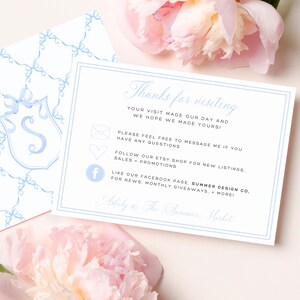 May include: A white card with light blue text and a light blue border. The card reads "Thanks for visiting" and includes contact information. A second card with a light blue bow pattern is visible. Pink flowers are in the background.