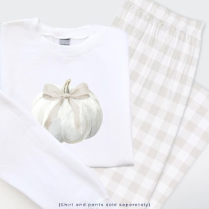 May include: White sweatshirt with a watercolor pumpkin design and a pair of beige and white plaid pajama pants. The pumpkin has a beige bow and stem. The text at the bottom says "(Shirt and pants sold seperately)".