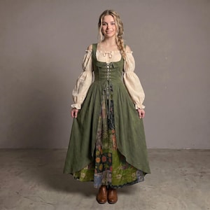 Könnte beinhalten: Ein langes olivgrünes Kleid mit einem korsettartigen Oberteil mit Schnürung vorne, getragen über einer cremefarbenen Bluse mit langen, weiten Ärmeln. Der Rock hat ein offenes Design, das einen gemusterten Unterrock mit Blumen- und Fruchtmotiven zeigt.