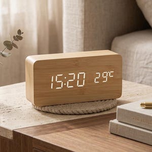 May include: A rectangular digital clock with a light wood grain finish. The front display features bright white LED numbers showing the time as 15:20 and the temperature as 29 degrees Celsius. The clock has rounded edges and a smooth surface.