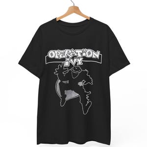 May include: A black short-sleeved t-shirt featuring a white graphic print. The design includes the text "OPERATION IVY" in a stylised font above a silhouette of a person wearing a hat and jumping, set against a circular background element.