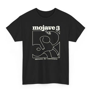 Puede incluir: Una camiseta negra de manga corta con un gráfico de líneas blancas de una persona tocando la guitarra. El texto "mojave 3" aparece sobre el gráfico y el texto "excuses for travellers" está impreso en blanco bajo la ilustración.