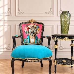 May include: An armchair with a black wooden frame, gold accents, and a bright turquoise seat. The backrest features a vibrant pink panel with a printed illustration of a leopard wearing a floral crown and a blue jacket, finished with gold nailhead trim.
