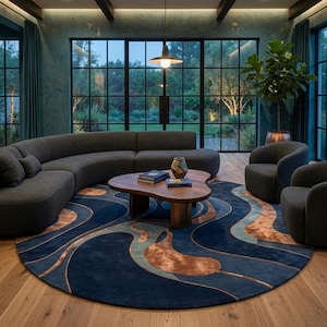 May include: A large round area rug featuring a fluid, abstract pattern in shades of deep navy blue, teal, and copper. The rug is placed on a light wood floor beneath a wooden coffee table, a curved dark gray sofa, and two matching armchairs.